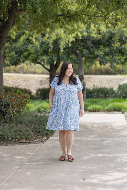 Woman wearing LuLaRoe Heidi babydoll dress in light blue medallion print with white detailing, button front, short sleeves, and flowy fit walking outdoors on a path