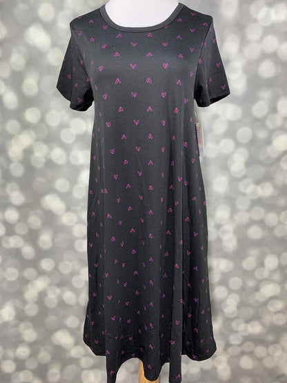 Front view of LuLaRoe Jessie dress on mannequin in black with allover pink mini heart pattern, short sleeves, and flowy swing fit against a blurred background