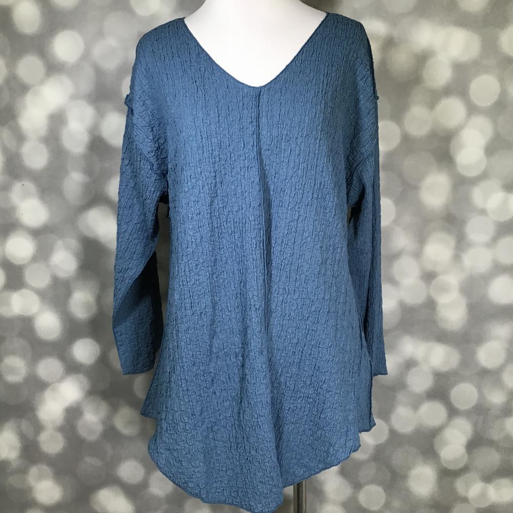 LuLaRoe Jolene V-neck tunic top in solid dusty blue bubble jacquard fabric displayed on a mannequin. Long sleeve, relaxed-fit tunic with gauze-like texture and high-low hem.