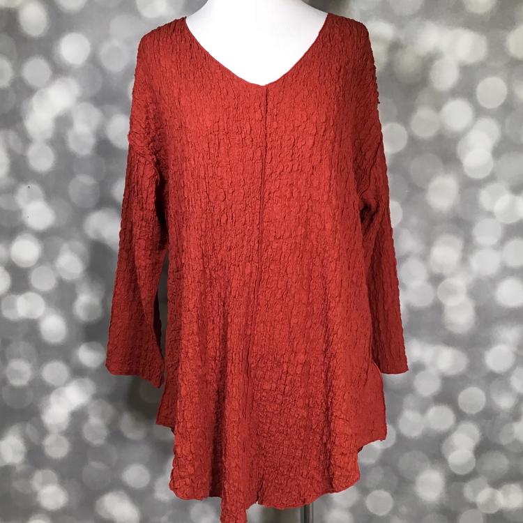 LuLaRoe Jolene V-neck tunic top in solid red ochre gauze bubble jacquard fabric displayed on a mannequin. Long sleeve, relaxed-fit tunic with textured finish in a rich red-orange hue.