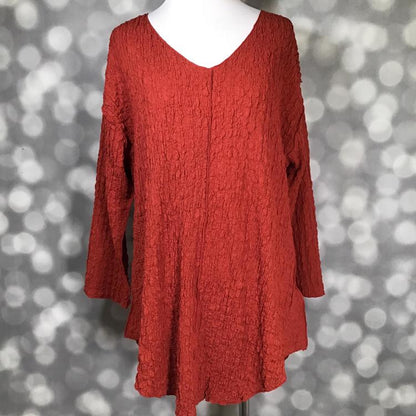LuLaRoe Jolene V-neck tunic top in solid red ochre gauze bubble jacquard fabric displayed on a mannequin. Long sleeve, relaxed-fit tunic with textured finish in a rich red-orange hue.