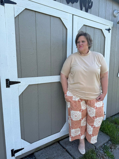 LuLaRoe Justine wide-leg pants in terracotta and cream geometric tile print, featuring elastic waistband and relaxed cropped fit, styled with a neutral top for an effortless everyday outfit on a woman standing in front of a wooden gate.