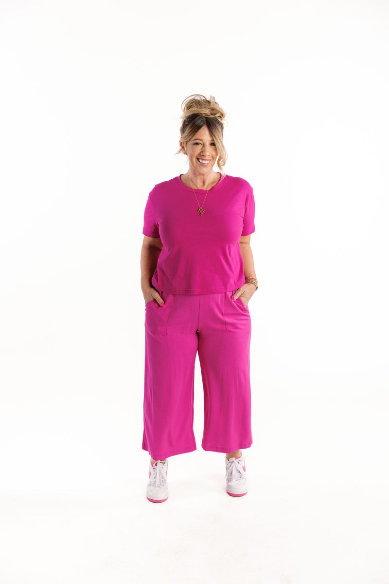 LuLaRoe Justine wide-leg pants in solid bright electric fuchsia pink, featuring elastic waistband, relaxed cropped fit, styled as a matching set with short sleeve top and sneakers on a white background
