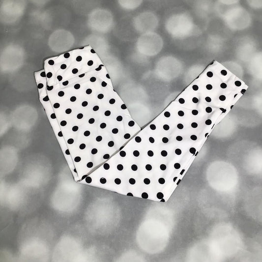 LuLaRoe Kids black and white polka dot leggings featuring classic black dots on a white background on a gray blurred background