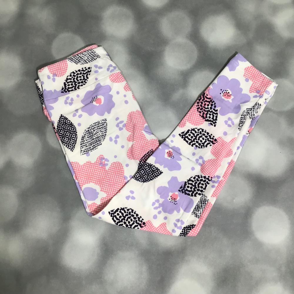 LuLaRoe Kids Lavender Patchwork Bloom leggings featuring lavender flowers, pink gingham shapes, black abstract leopard patterns on a cream background on a blurred background