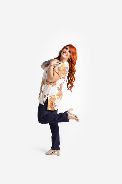 LuLaRoe Leah top in cream with golden amber floral print and brown leaf accents, relaxed fit women’s boutique fall floral top on a woman with dark pants posing on a white background