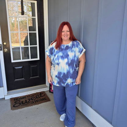 LuLaRoe Leah top in indigo cloud wash tie-dye print featuring blue and ivory abstract pattern, relaxed fit women’s boutique casual top on a woman standing outside a house with a 'Home Sweet Home' doormat.