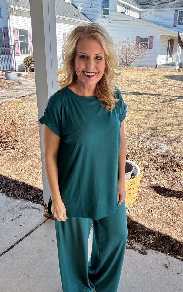 LuLaRoe Leah top in solid deep evergreen green, relaxed fit women’s casual top with soft drape fabric, versatile everyday layering piece on a woman standing on a porch with a house in the background