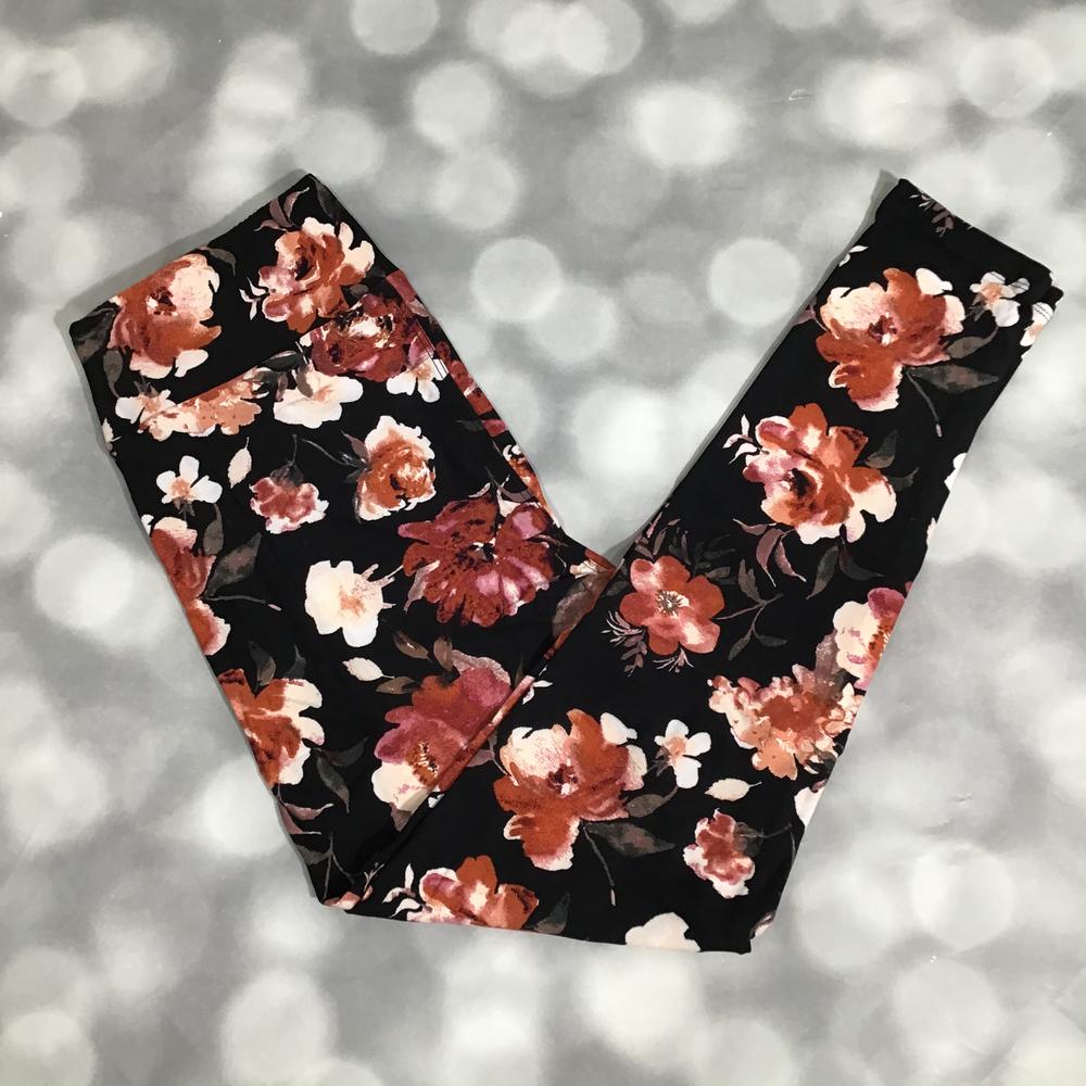 Black LuLaRoe leggings featuring watercolor floral blooms in mocha brown, rust, mauve, blush pink, and ivory tones photographed folded flat against a silver bokeh background.