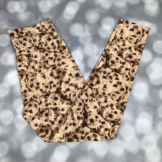 LuLaRoe leggings with an allover chocolate chip cookie print in warm brown tones, shown in flat lay on a blurred background