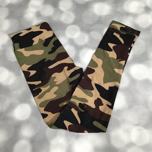 LuLaRoe leggings in classic woodland camo print displayed flat on a soft gray bokeh background. Features earthy green, tan, brown, and black camo shapes in a smooth, stretchy fabric.