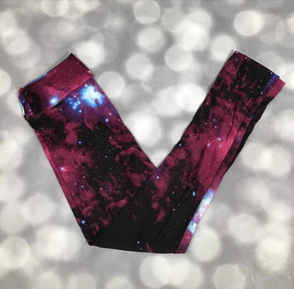 LuLaRoe leggings with crimson nebula galaxy print featuring red space clouds, blue star clusters, and black cosmic background on a blurred gray background