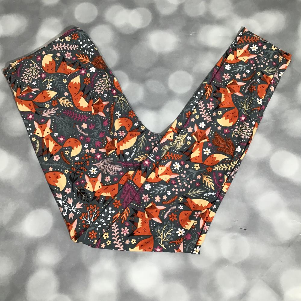 LuLaRoe fox print leggings featuring illustrated orange foxes with floral and leafy details on a charcoal gray background, photographed laid flat on a light gray backdrop.