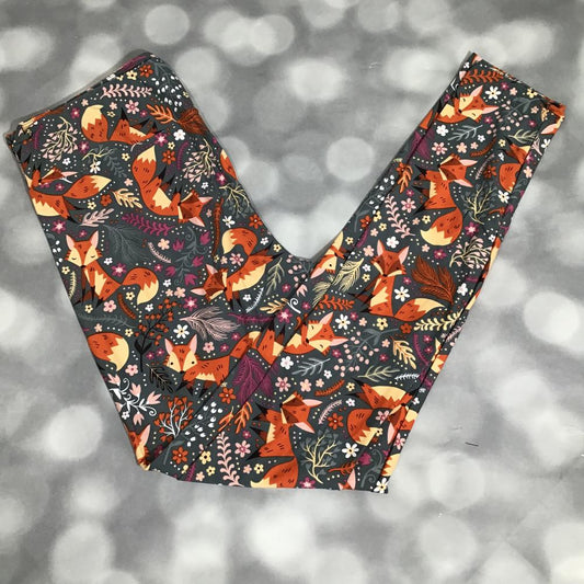 LuLaRoe fox print leggings featuring illustrated orange foxes with floral and leafy details on a charcoal gray background, photographed laid flat on a light gray backdrop.