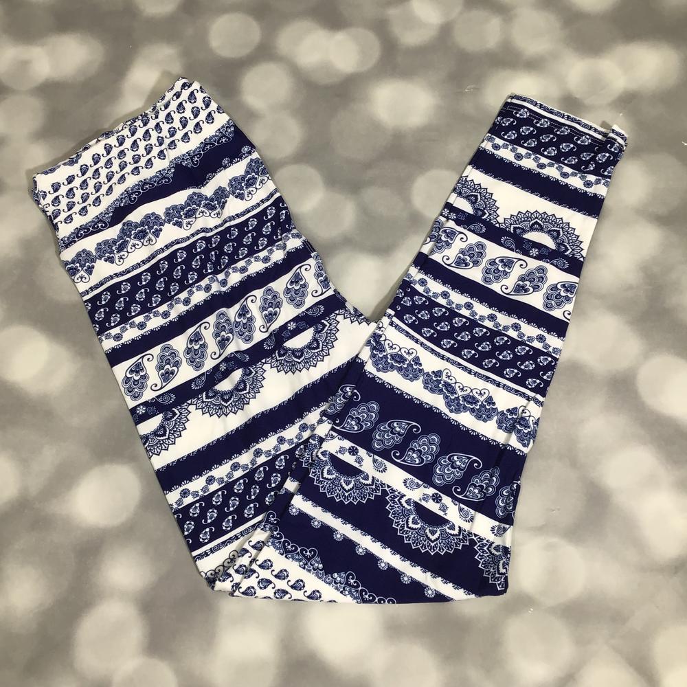 Blue and white LuLaRoe leggings featuring mixed paisley, mandala, and bohemian tapestry stripe patterns photographed folded flat against a silver bokeh background.