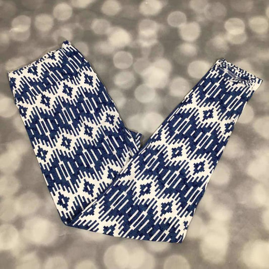 LuLaRoe leggings featuring an indigo blue and white geometric ikat-inspired pattern with southwestern diamond motifs and linear tribal details. Women's patterned leggings with a bold boho geometric design on a blurred gray background.