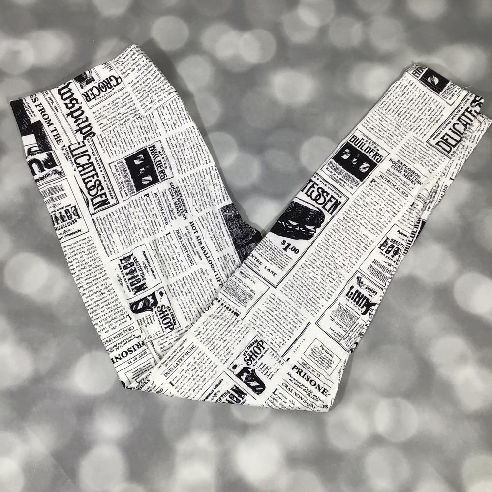 LuLaRoe black and white newspaper print leggings featuring vintage headlines, article columns, and typographic graphics, photographed laid flat on a light gray background.
