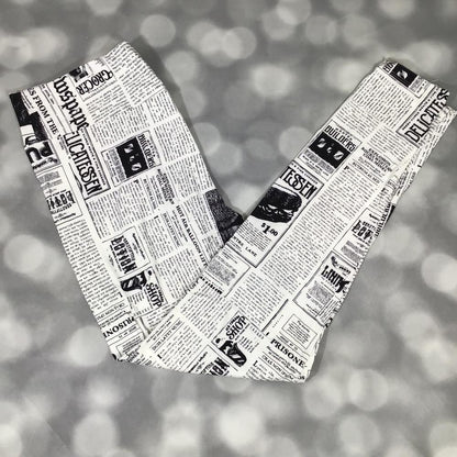 LuLaRoe black and white newspaper print leggings featuring vintage headlines, article columns, and typographic graphics, photographed laid flat on a light gray background.