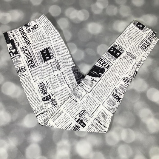 LuLaRoe black and white newspaper print leggings featuring vintage headlines, article columns, and typographic graphics, photographed laid flat on a light gray background.