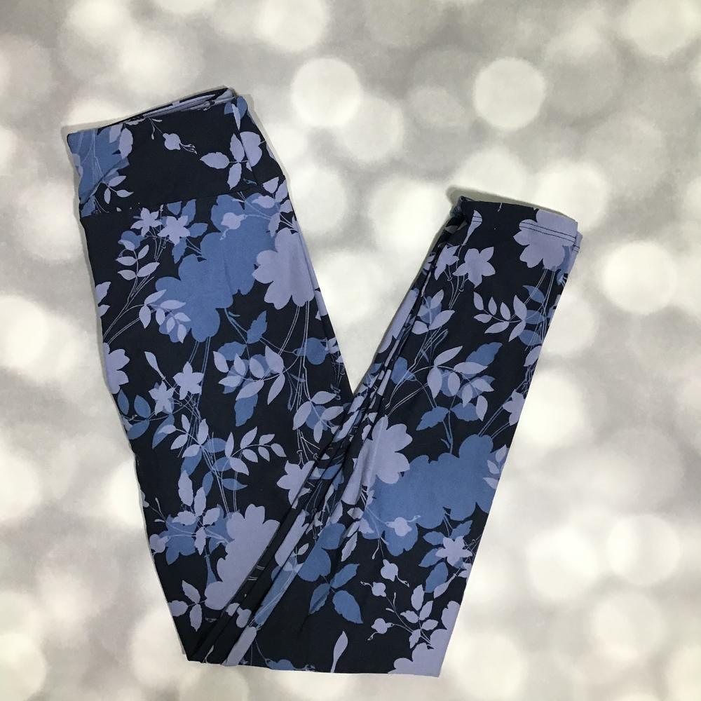 LuLaRoe leggings with dark black background and blue floral botanical pattern, shown flat lay with soft stretch fabric on a light background