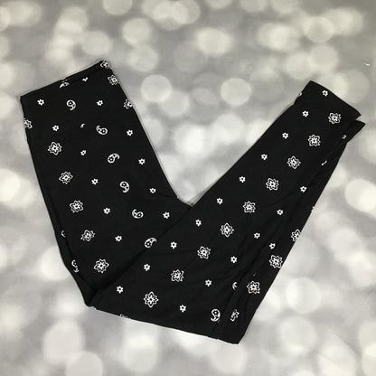 LuLaRoe leggings featuring a black background with scattered white daisy flowers and paisley-inspired floral motifs. Women's buttery soft printed leggings with monochrome floral pattern suitable for casual outfits, layering, lounging, and everyday wear on a blurred gray background