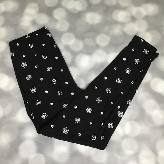 LuLaRoe leggings featuring a black background with scattered white daisy flowers and paisley-inspired floral motifs. Women's buttery soft printed leggings with monochrome floral pattern suitable for casual outfits, layering, lounging, and everyday wear on a blurred gray background