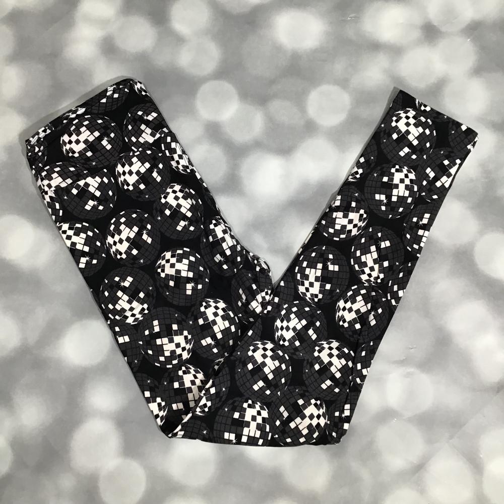 LuLaRoe leggings with a black background and repeating silver disco ball pattern, photographed flat with crossed legs on a textured gray background