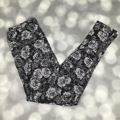 LuLaRoe leggings featuring an allover ivory rose floral print with a textured etched design on a black background, laid flat on a light gray surface.