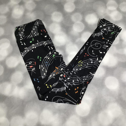LuLaRoe leggings laid flat featuring a black background with white musical staff lines and colorful music notes in green, orange, red, blue, and yellow on a blurred background
