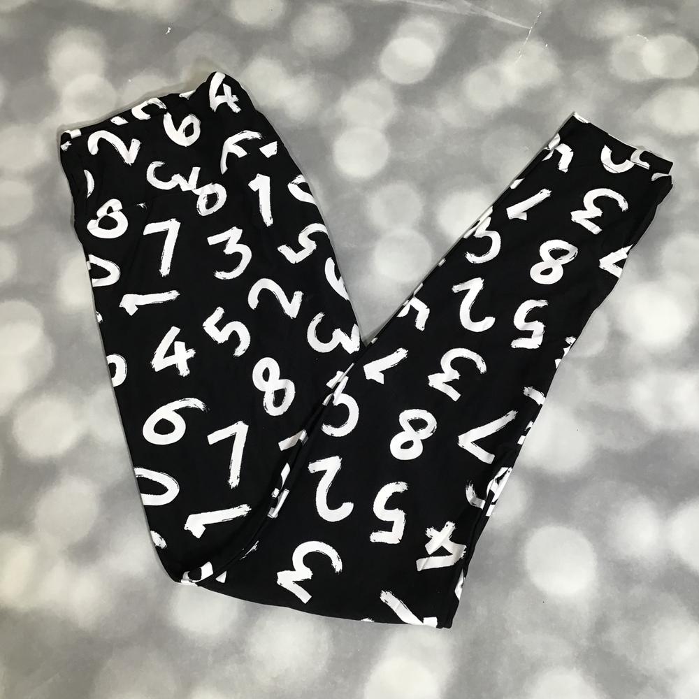Black LuLaRoe leggings featuring oversized white abstract painted numbers in a bold monochrome graphic print photographed folded flat against a silver bokeh background.