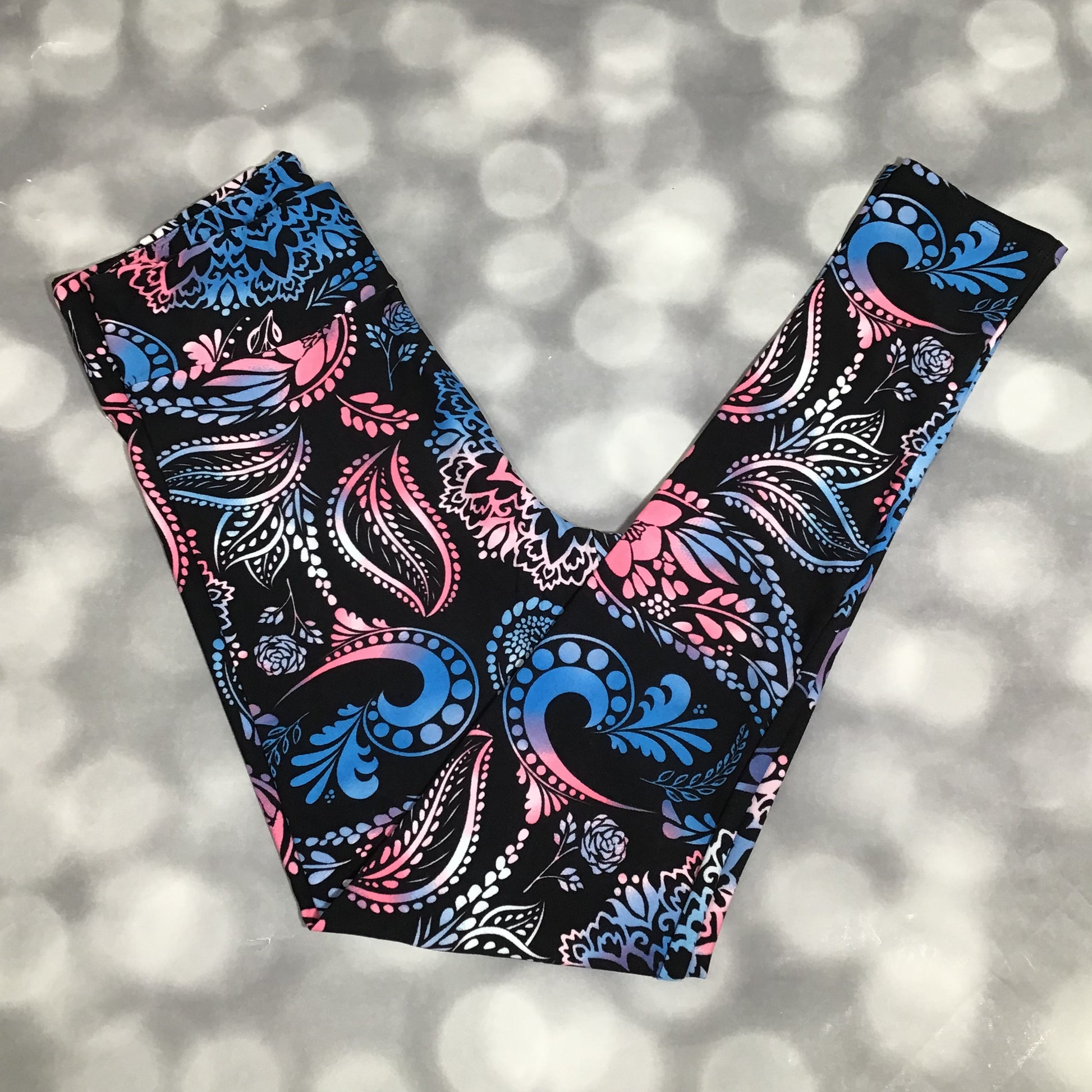 LuLaRoe leggings featuring a black background with pink and blue paisley and floral swirl patterns in an all-over ornamental print on a blurred background