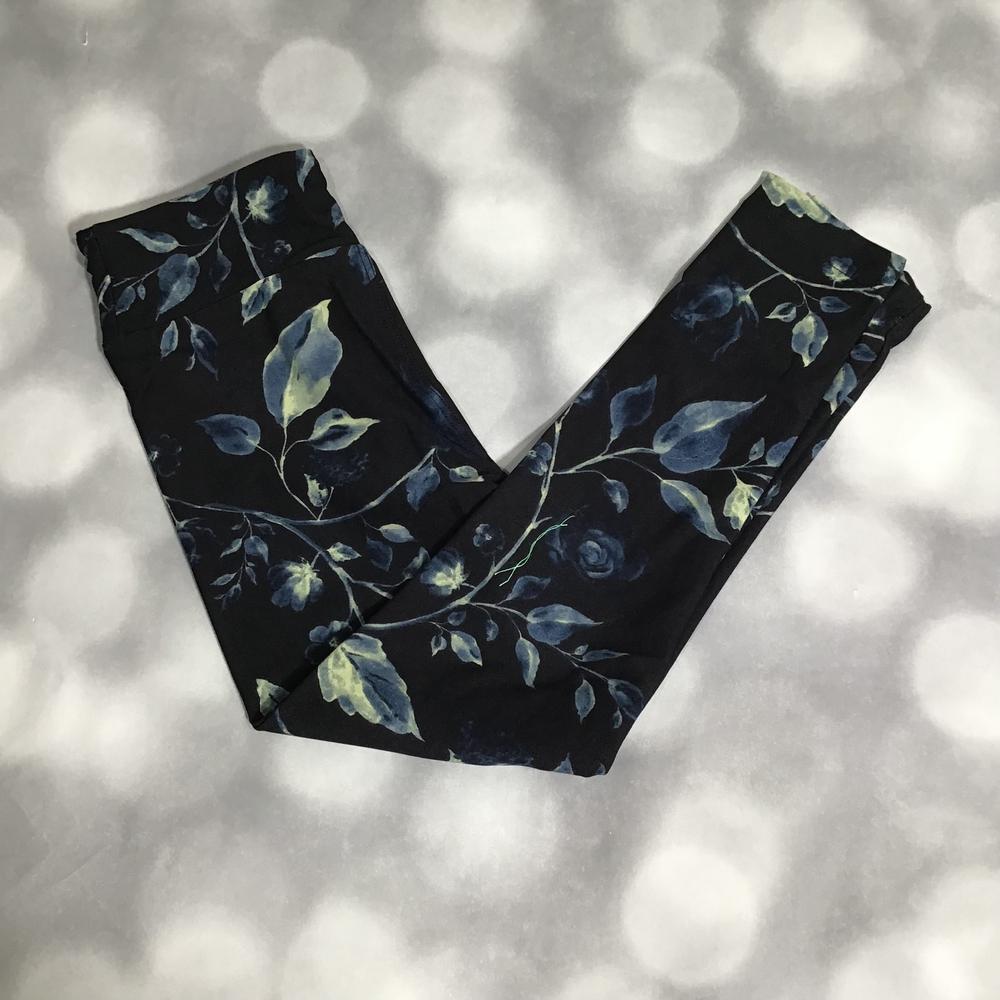 LuLaRoe leggings with dark black background featuring blue and sage green leafy botanical vine print a blurred gray bokeh background