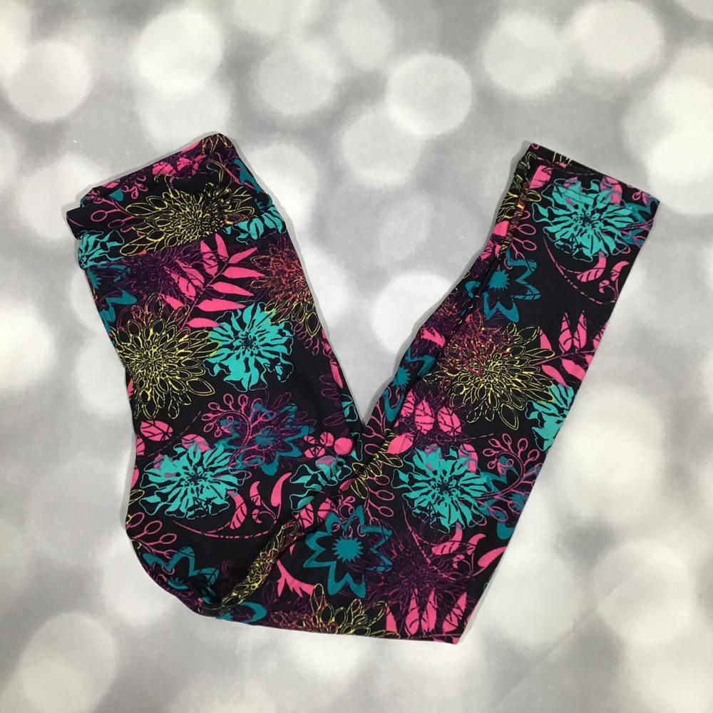 LuLaRoe leggings featuring a black background with vibrant turquoise, hot pink, magenta, purple, and chartreuse floral blooms and abstract botanical designs. Women's colorful floral leggings with a bold artistic statement print on a gray blurred background