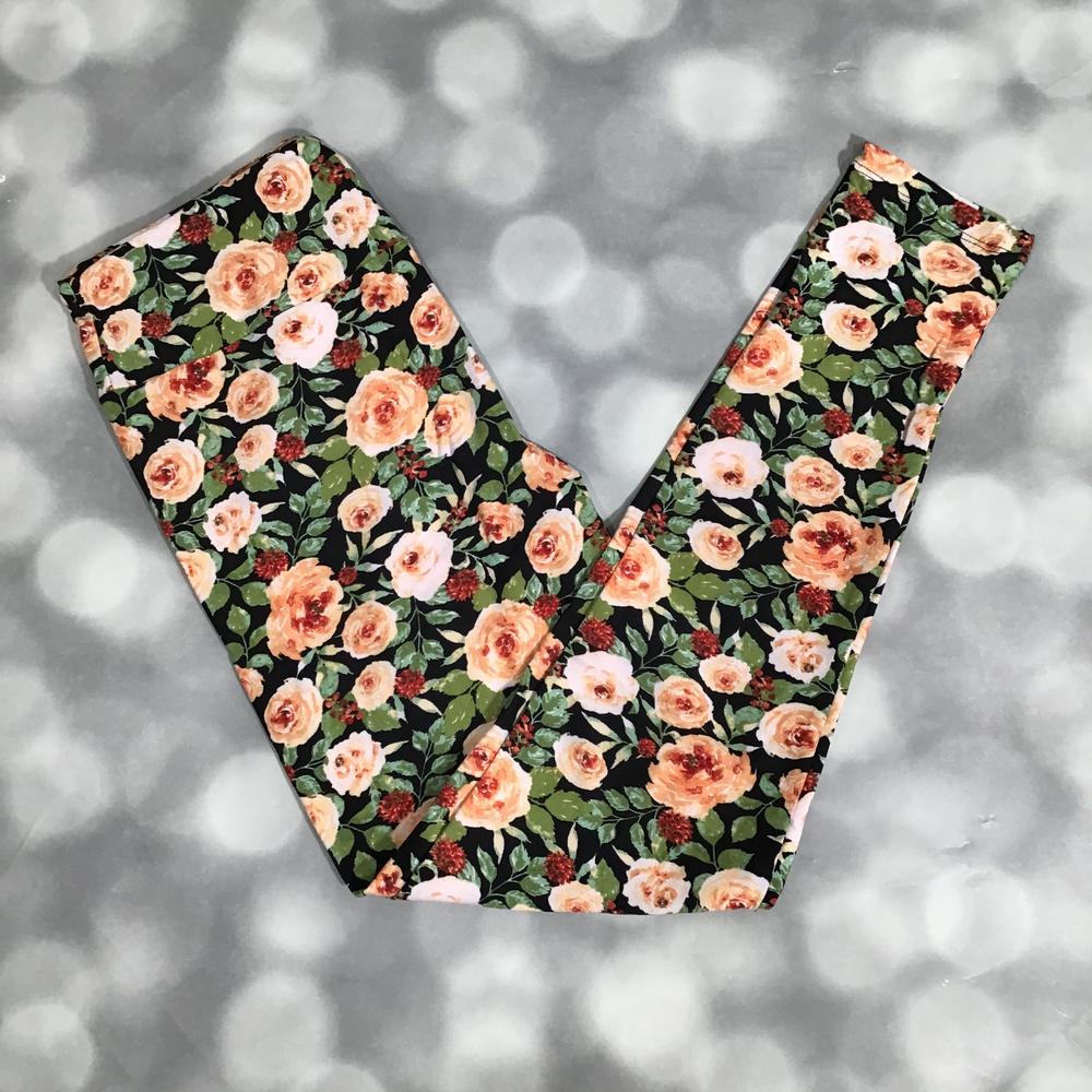 LuLaRoe leggings featuring peach and blush rose florals with green leaves on a black background, laid flat on a light gray surface.