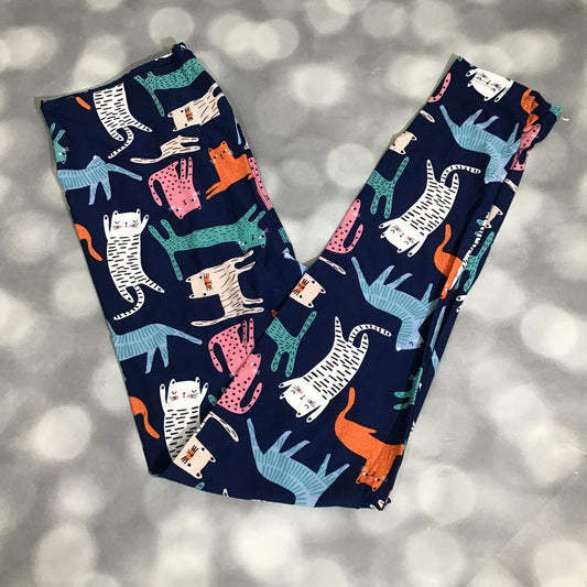 LuLaRoe leggings laid flat with a navy background featuring colorful whimsical cats in teal, pink, coral, cream, and aqua in a playful all-over cat print.