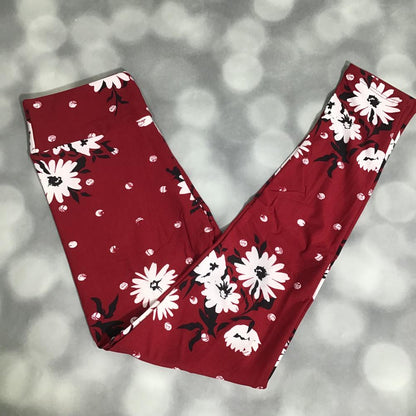 LuLaRoe leggings laid flat featuring a bold scarlet red background with large white daisy flowers, black leaf accents, and scattered white dots on a blurred gray background
