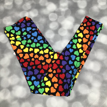 LuLaRoe leggings featuring a black background with multicolored rainbow heart shapes arranged in an all-over repeating pattern on a blurred gray background