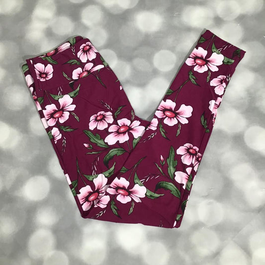 Berry-magenta LuLaRoe leggings featuring oversized blush pink hibiscus-style flowers with green leaves photographed folded flat against a silver bokeh background.