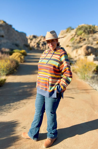 Woman wearing a multicolor striped LuLaRoe Lexi Hooded Fleece Sweatshirt with side slits, long raglan sleeves, and ribbed trim, styled outdoors with jeans.