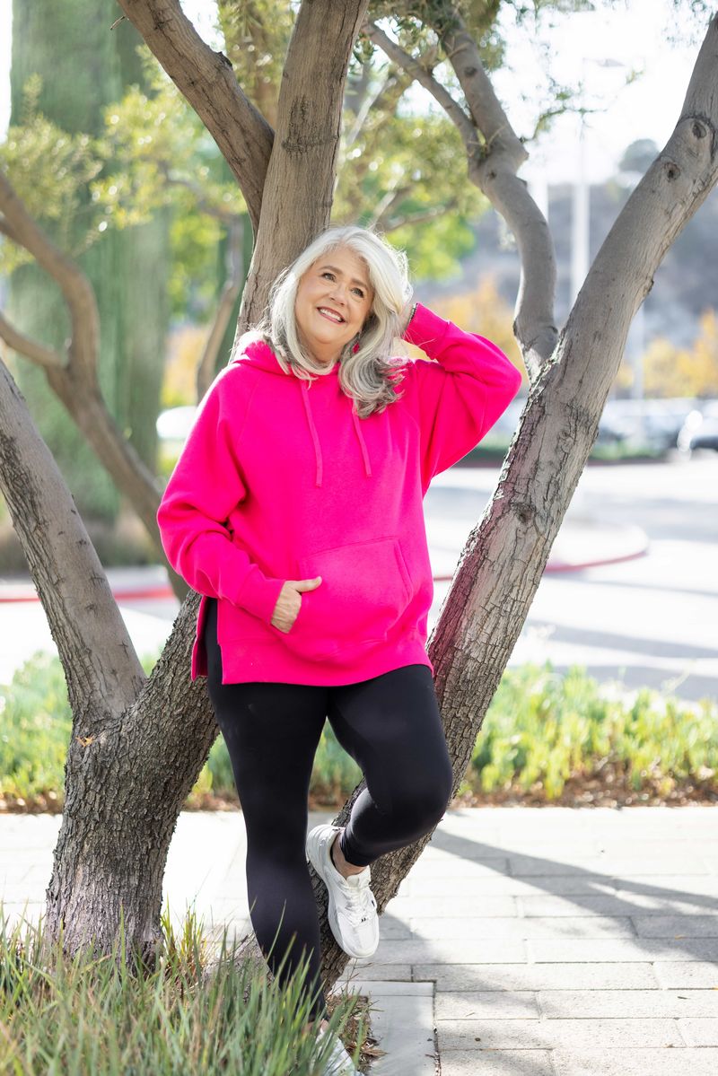 Lexi Hooded Fleece Sweatshirt in solid hot pink displayed on a model outdoors. Long-sleeve relaxed-fit hoodie with kangaroo pocket, drawstring hood, side slits, and ribbed cuffs and hem.