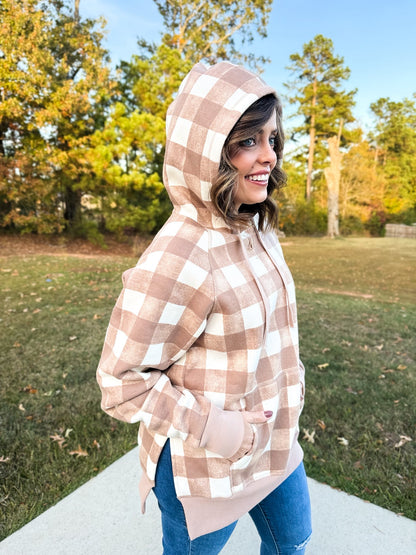 Woman wearing a tan and cream buffalo check LuLaRoe Lexi Hooded Fleece Sweatshirt with side slits, raglan sleeves, and kangaroo pocket, styled outdoors with jeans.