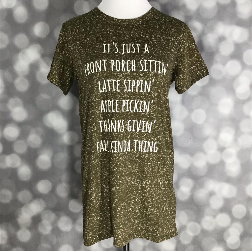 LuLaRoe Liv T in heathered olive with white fall-themed text graphic” | “Front view of LuLaRoe Liv T on mannequin featuring heathered olive knit fabric and white text that reads ‘It’s just a front porch sittin’, latte sippin’, apple pickin’, thanks givin’, fall kinda thing' on a blurred background