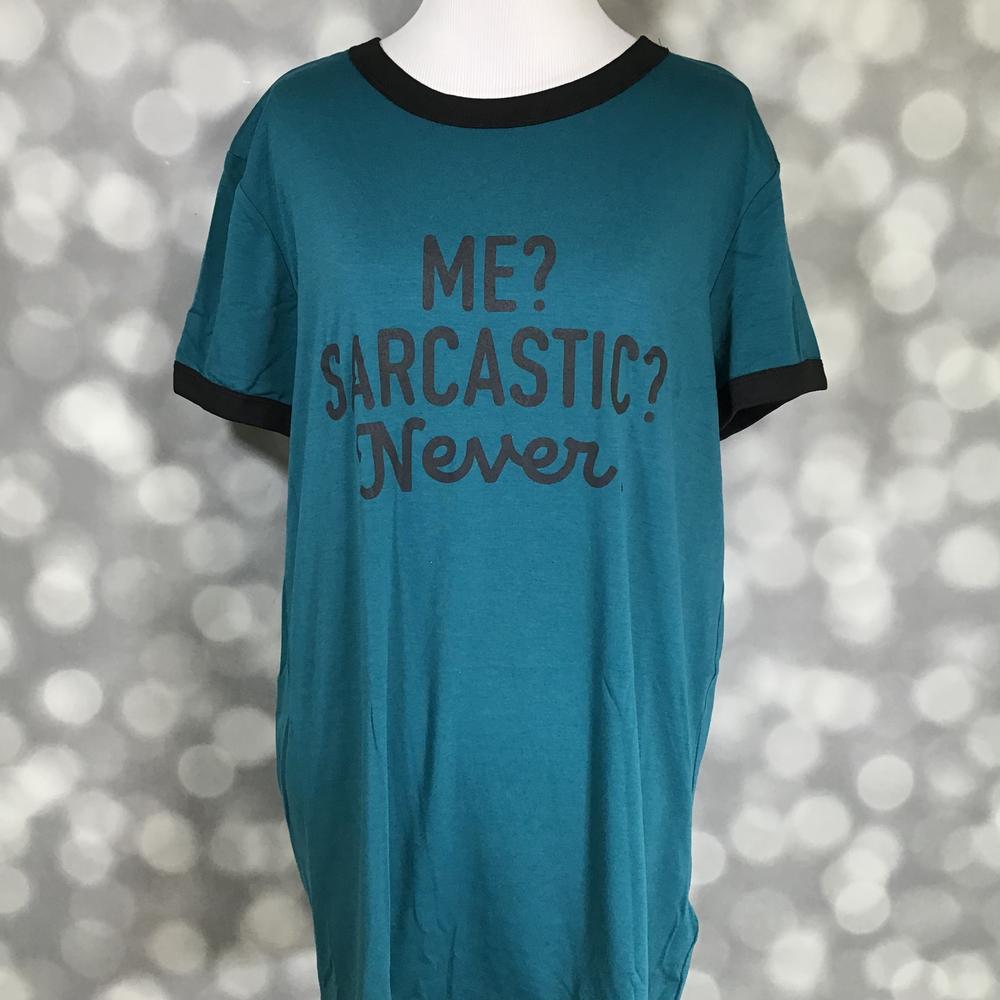 LuLaRoe Liv T in teal with black contrast trim and ‘Me? Sarcastic? Never.’ text graphic” | “Front view of LuLaRoe Liv T on mannequin featuring teal body with black collar and sleeve trim and playful ‘Me? Sarcastic? Never.’ text design on a blurred background
