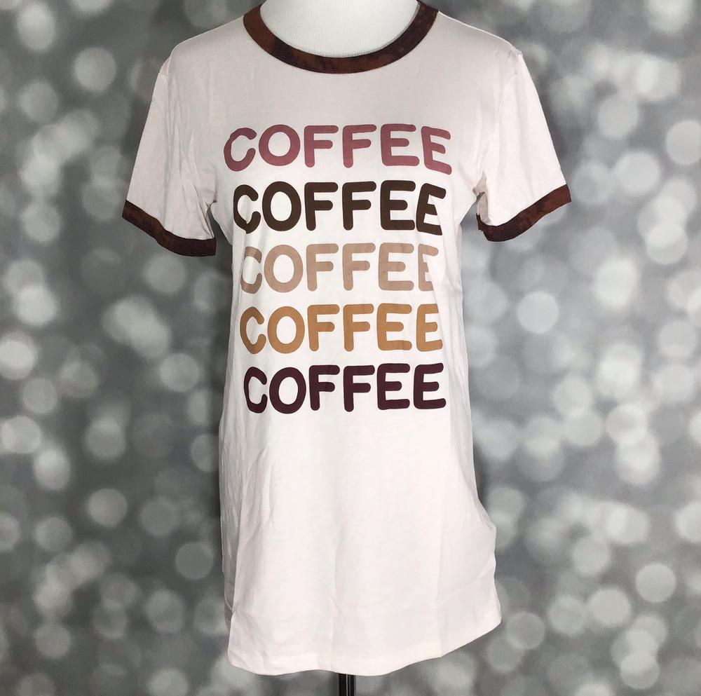 Front view of LuLaRoe Liv T on mannequin featuring white body with COFFEE text in gradient brown and pink tones and contrast trim on a blurred background