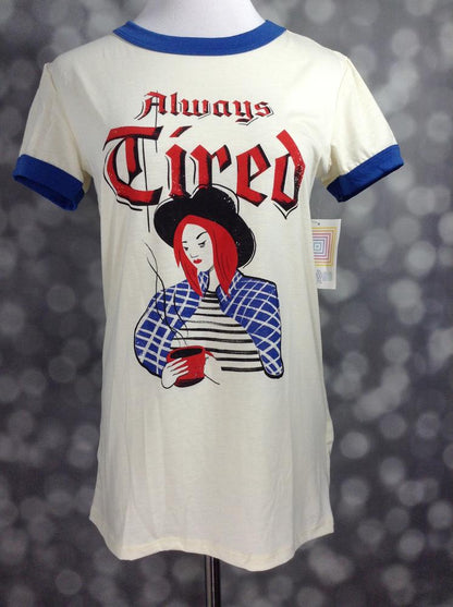 LuLaRoe Liv Tee ivory shirt with 'Always Tired' coffee graphic and blue ringer trim on a mannequin against a blurred background