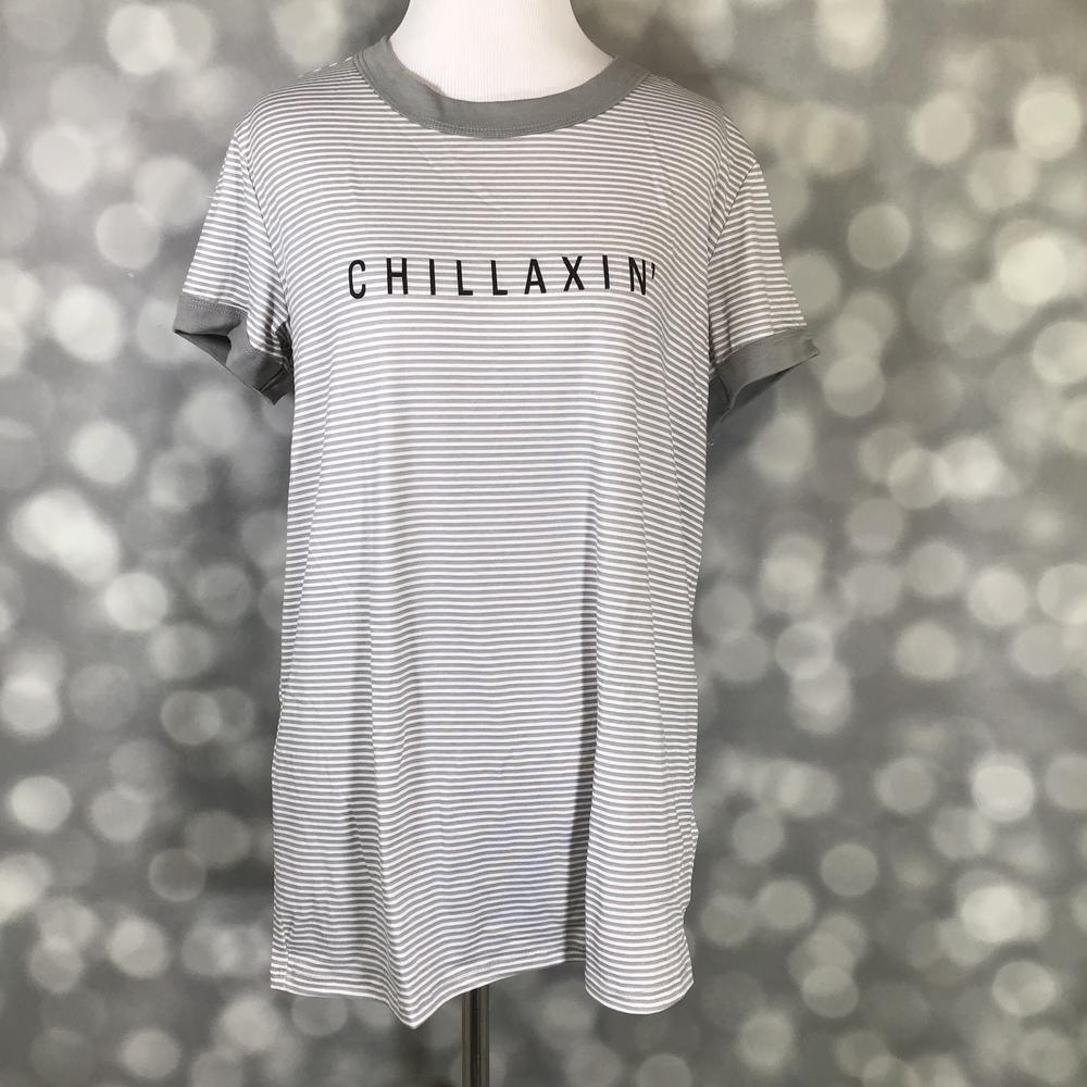 LuLaRoe Liv Tee featuring thin gray and white horizontal stripes with "CHILLAXIN" graphic text across the front. Women's casual graphic t-shirt with a relaxed fit, crew neckline, and comfortable everyday style on a mannequin against a blurred background