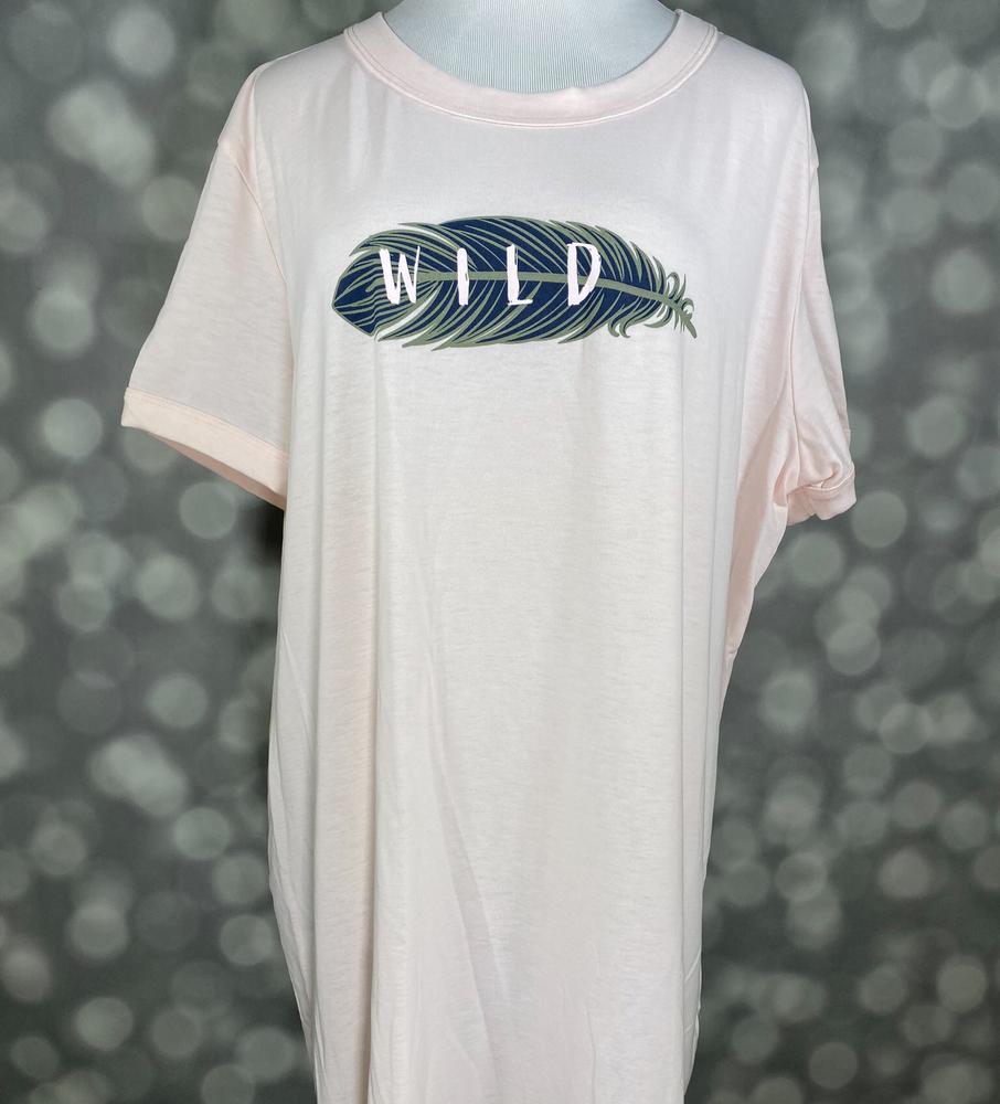 LuLaRoe Liv Tee blush pink graphic shirt featuring a navy and teal feather with the word “WILD” printed across the feather on a relaxed fit tee on a blurred background