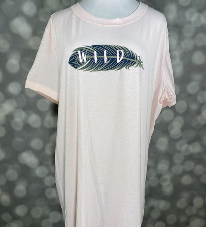 LuLaRoe Liv Tee blush pink graphic shirt featuring a navy and teal feather with the word “WILD” printed across the feather on a relaxed fit tee on a blurred background