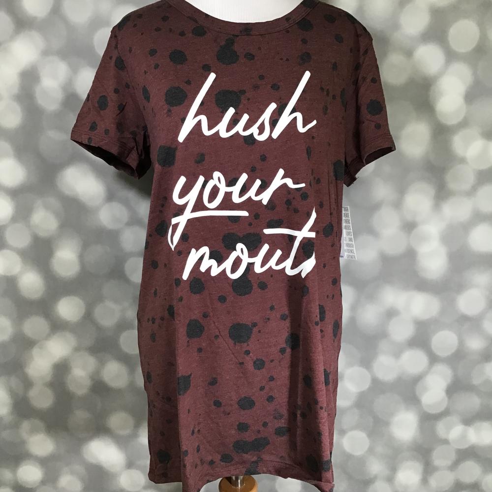 LuLaRoe Liv tee on mannequin featuring a burgundy heather background with black splatter detail and white “hush your mouth” script graphic on the front.