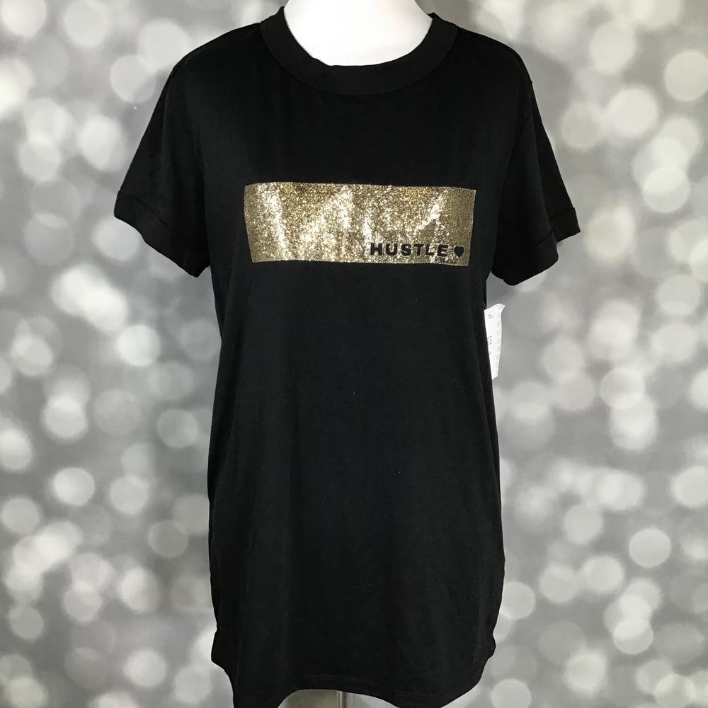 LuLaRoe Liv Tee in black featuring a metallic gold "Hustle" graphic across the front. Women's relaxed fit graphic t-shirt with motivational typography and modern casual styling for everyday wear, work-from-home outfits, and entrepreneur-inspired fashion. on a blurred background